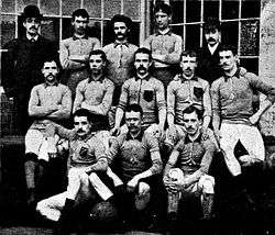 A group of thirteen men, eleven in association football attire typical of the late nineteenth century and two in suits and bowler hats