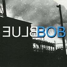 A black-and-white silhouette image of an industrial factory. Large volumes of smoke are visible in the sky. Uppercase white mirrored text in the center reads "Blue" (stylized as "ƎU⅃ᗺ"); uppercase blue text next to it reads "Bob", with black outline around the text.