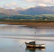 A fishing boat at anchor in the estuary, with mudflats and mountains in the background