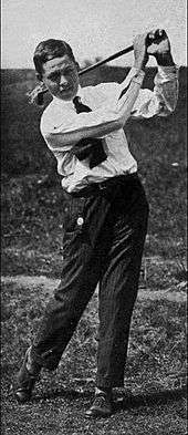 A young man in a white shirt, dark tie and dark pants completing a right-handed golf swing