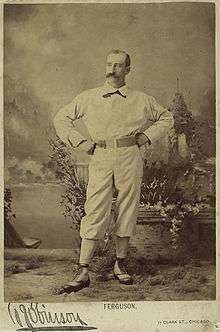 A portrait of man in a baseball uniform, standing with his hand on his hips, facing slightly to the right and up.