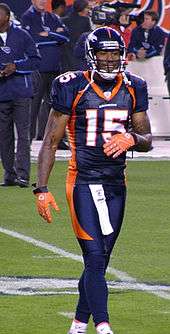 A African-American football player dressed in uniform and protective gear walks on the field.