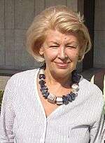 A photo of Ewa Braun wearing a striped blouse and a necklace with blue and grey stones.