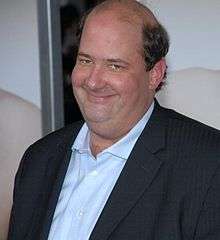 A smiling, heavyset, balding man wears a suit jacket and blue shirt.