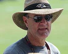Billick wearing sunglasseds and a wide-brimmed straw hat with a Ravens logo on the hatband