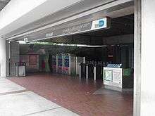 The entrance to a metro station featuring a large number of turnstiles and a sign above that reads "Brickell".