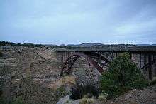A dusk picture of a steel arch bridge spanning a deep canyon. In the background the corner of a 2nd bridge is visible.