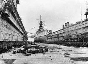 A view of a large warship from the floor of a dry dock