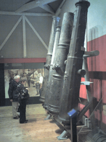 A view of four very large cannons leaning towards the inside wall of a building with a high ceiling