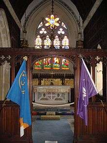alter of a neo-Gothic church, showing colourful stained glass windows, with two flags posted in the foreground