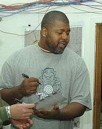 Candid waist-up photograph of Cox wearing a grey t-shirt and apparently signing an autograph