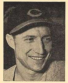 A man wearing a dark baseball cap with a "C" on the center smiles and looks to the right.