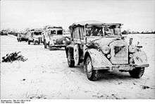 a black and white photograph of a column of vehicles covered in snow