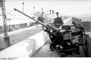 single barrelled gun with sentry behind large commercial ships in the background