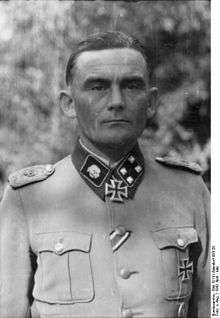 A black-and-white photograph of a man wearing a military uniform and neck order in shape of an Iron Cross. His hair is combed back and his facial expression is determined.