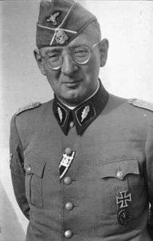 A man wearing a military uniform, side cap and glasses.