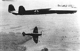 Twin-engined, twin-finned aircraft in flight with single-engined aircraft in lower background