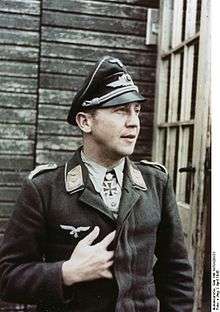 Color portrait of a man wearing a peaked cap, military uniform with an Iron Cross displayed at his neck.