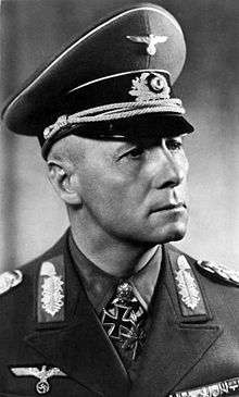 The head and shoulders of an elderly man, shown in semi-profile. He wears a peaked cap and a military uniform with an Eagle above his right and various military decorations above left breast pocket, and an Iron Cross displayed at the front of his shirt collar. His facial expression is a determined; his eyes are looking into the distance to the left of the camera.