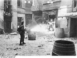 A black and white photograph of a German Verbrennungskommando soldiers using a flamethrower to set fire to ruins of a Warsaw building.