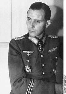 Black-and-white portrait of a man in semi profile wearing a military uniform with various military decorations, his dark hair is parted and combed back.