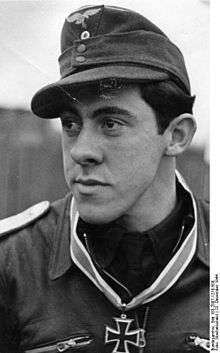 A man wearing a military uniform and field cap with an Iron Cross displayed at the front of his uniform collar.
