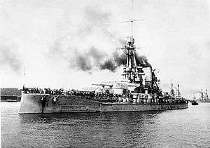 A large gray battleship sits in harbor