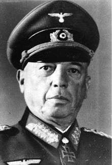 Black-and-white portrait of an older man wearing a peaked cap, military uniform with an Iron Cross displayed at his neck.