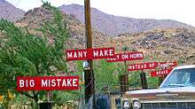 A set of 6 white-on-red signs with white block text along the side of a road, reading in order "BIG MISTAKE", "MANY MAKE", "RELY ON HORN", "INSTEAD OF BRAKE", and, stylized, "Burma-Shave".