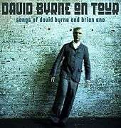Tour poster featuring Byrne posing in front of a teal brick wall with stylized text reading "David Byrne on Tour / Songs of David Byrne and Brian Eno".