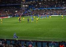 Chelsea (blue) and Barcelona players (yellow) leave the pitch at the end of the first half of their semi-final second leg at Stamford Bridge. The referee is talking to two Barcelona players.
