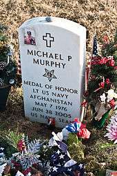 A military grave stone with an image of a man with a cross next to it. Also shows the name of the individual and info about them with an image of the Medal of Honor.