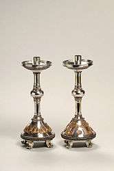 Pair of silver candlesticks, ornately decorated with heart shapes and scroll patterns.