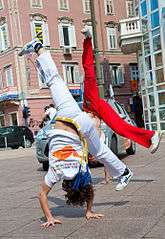 Two Croatian practitioners of the Brazilian martial art capoeira in the middle of doing a cart wheel on a public sidewalk.