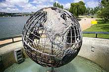 A large metal wire globe depicting the travels of Captain Cook stands on a concrete platform on the shore of the lake, amidst landscaped parks.