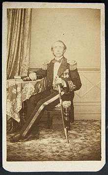 Full-length portrait of seated man at table wearing military uniform and sword