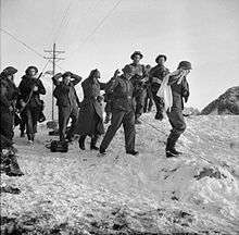 four Germans one with a white g=flag surrounded by British troops crossing a snow-covered landscape