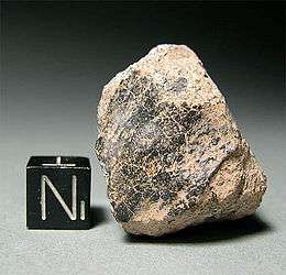 Lump of rock shown next to a much smaller cube to demonstrate relative size.