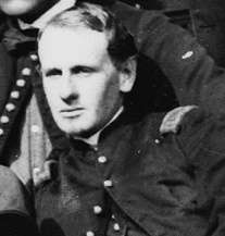Head of a clean-shaven young man leaning to the side and wearing a military jacket with a single button buttoned near the neck.
