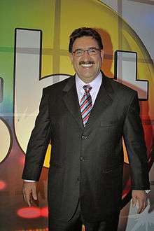 Smiling, middleaged, darkhaired mustachioed man, wearing glasses and a suit