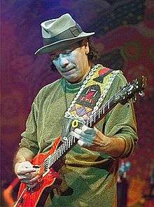Older man playing a guitar and wearing a green shirt and hat