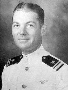 Head and shoulders of a white man with wavy hair, wearing a white military jacket with shoulder boards and a winged pin on the left breast.