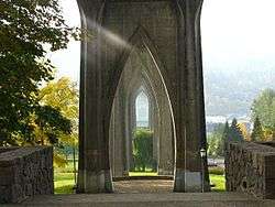A series of arches on the underside of a bridge; trees and a manicured lawn are visible in the background.