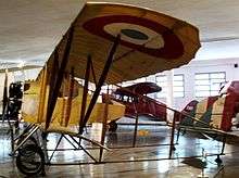A small yellow biplane with steel latticework serving as the fuselage between the cockpit and tail