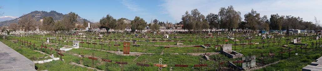 Rows of graves with metal crosses for headstones, a mountain in the distance
