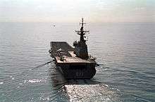 A small aircraft carrier photographed from behind as she sails across calm waters