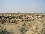 Ruins of former buildings in a desert setting consisting of low walls with a fishnet pattern.