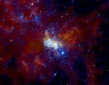 A white, glowing, cloudlike feature lies surrounded by bright blue stars in a brownish, golden nebula