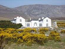 Charles Boycott's house on Achill Island. It is a large white house with two storeys. The mountainous terrain on the island is seen in the background.