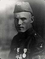 Head and shoulders of a low-ranking U.S. soldier in a garrison cap wearing three large medals on his chest. He has an intimidating expression, and his eyes almost glare at the camera.